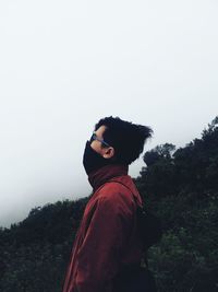 Side view of young man looking at camera against sky
