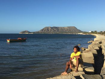 Man sitting on rock by sea against sky