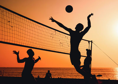 Silhouette people playing soccer on beach against sky during sunset