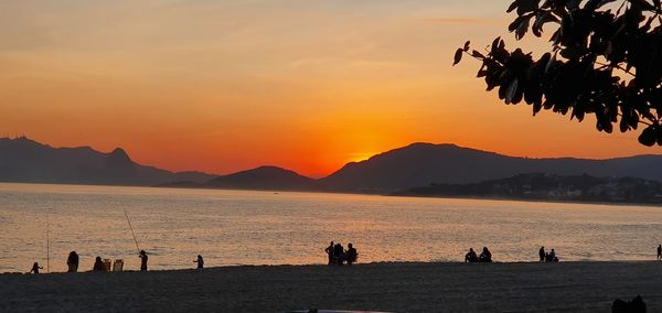 Silhouette people on beach against sky during sunset