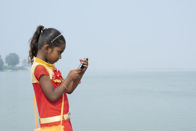 Side view of girl using mobile phone while standing against sea