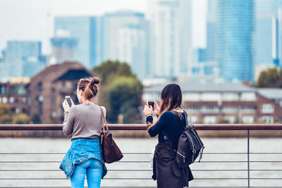 Rear view of friends sitting on railing in city