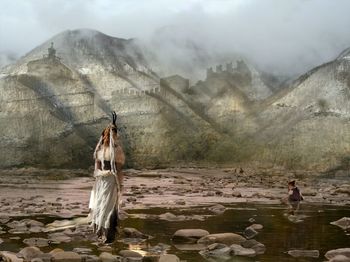 People standing on rock by lake against mountain range