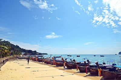 People and boats at beach against blue sky