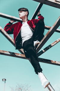 Low angle view of man sitting on metal against sky