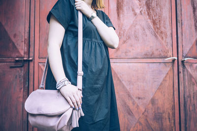 Midsection of woman holding umbrella standing against wall