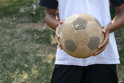 Midsection of man holding ball while standing on soccer field