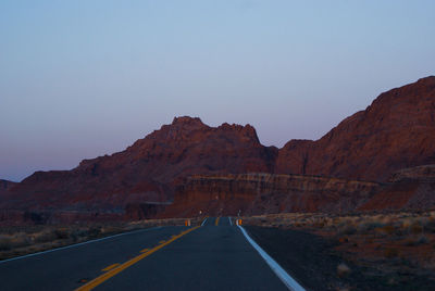 Road leading towards mountain against clear sky