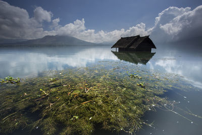 View of abandoned hut in water against cloudy sky