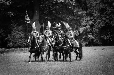 Men riding horses on field against trees