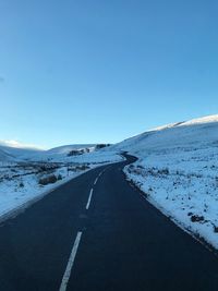 Road on snow covered landscape against clear blue sky