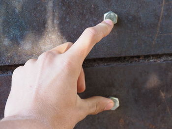 Cropped image of hand touching screws mounted on metal