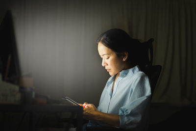 Side view of young woman using phone while sitting on table