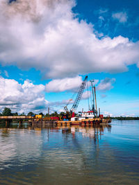 Cranes on pier over river against sky