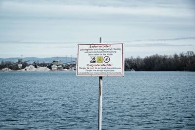 Information sign by lake against sky