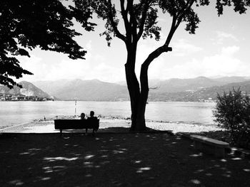 Silhouette people sitting on bench by sea against sky