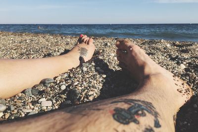 Low section of man and woman sitting on shore at beach