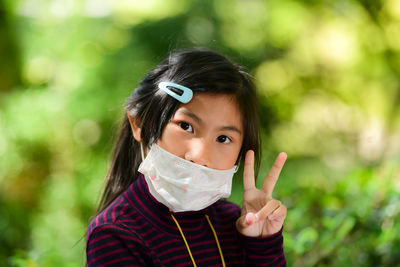 Close-up portrait of girl wearing pollution mask while gesturing peace sign