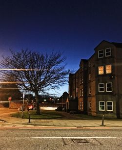 Road by trees and buildings against blue sky at night