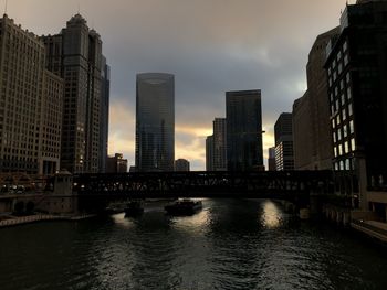 View of buildings by river against cloudy sky