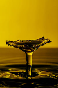 Close-up of water splashing on glass against yellow background