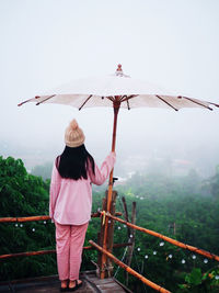 Rear view of woman holding umbrella against sky