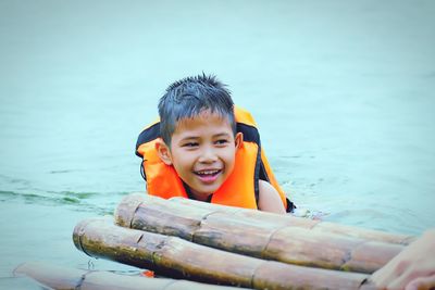 Smiling boy wearing life jacket swimming in lake