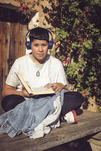 Young student reading and listening to music sitting in the garden