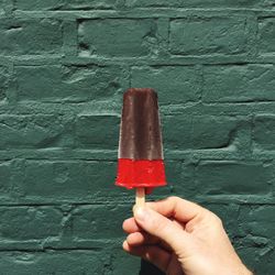 Cropped hand holding popsicles against green wall