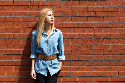 Woman looking away while standing by brick wall