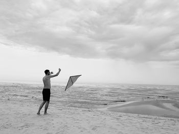Full length of man flying kite while standing at beach against sky