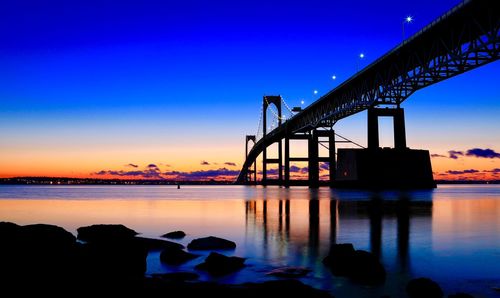 Silhouette bridge over river against sky during sunset