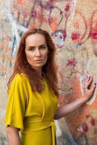 Portrait of woman standing by graffiti wall