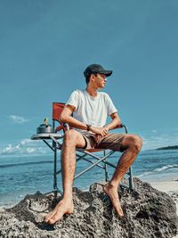 Man sitting on rock at beach against sky