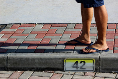 Low section of man standing by number 42 on sidewalk