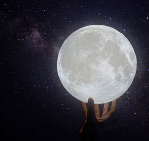 Low angle view of hand holding moon at night