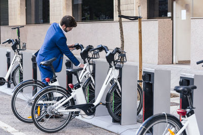 Young bearded businessman in elegant clothes parking modern bike on city street in back lit