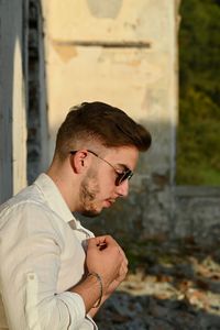 Side view of young man wearing eyeglasses against wall