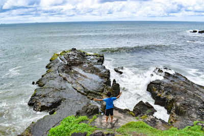 Rear view of boy on rocks by sea against sky