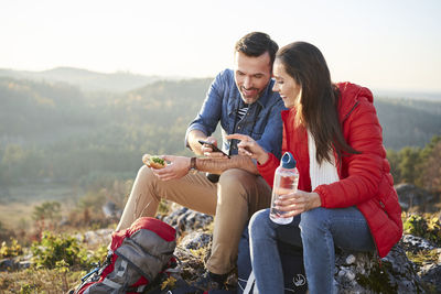 Happy couple on a hiking trip in the mountains taking a break looking at cell phone