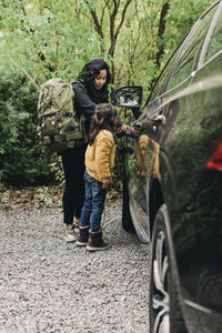 Mid adult woman teaching daughter to charge electric car at charging station