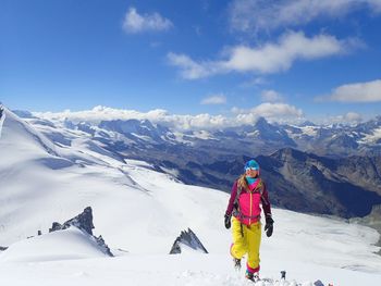 Woman walking on snowcapped mountain against sky
