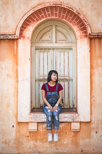 Full length of young woman sitting on window sill in old building