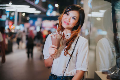 Portrait of young woman standing against illuminated traditional clothing