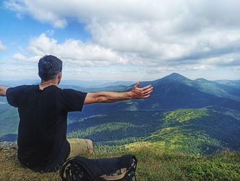 Rear view of man standing on mountain against sky