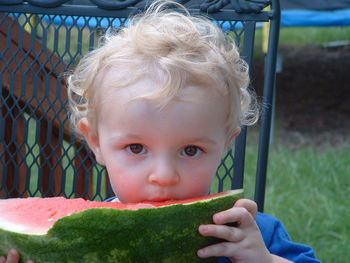 Cute baby eating watermelon while sitting on chair at yard