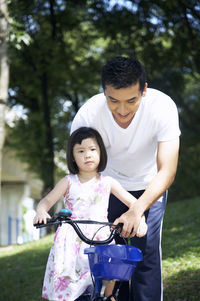 Father assisting daughter cycling at park