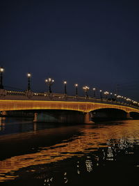 Illuminated bridge over river against sky in city at night