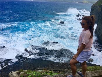 High angle view of woman standing on cliff against blue sea