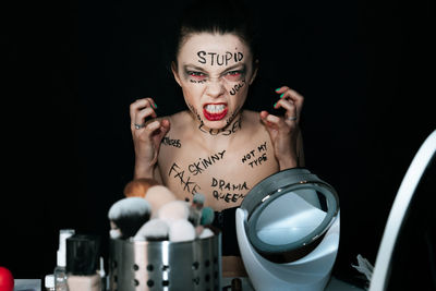 Portrait of angry woman with text on body sitting against black background
